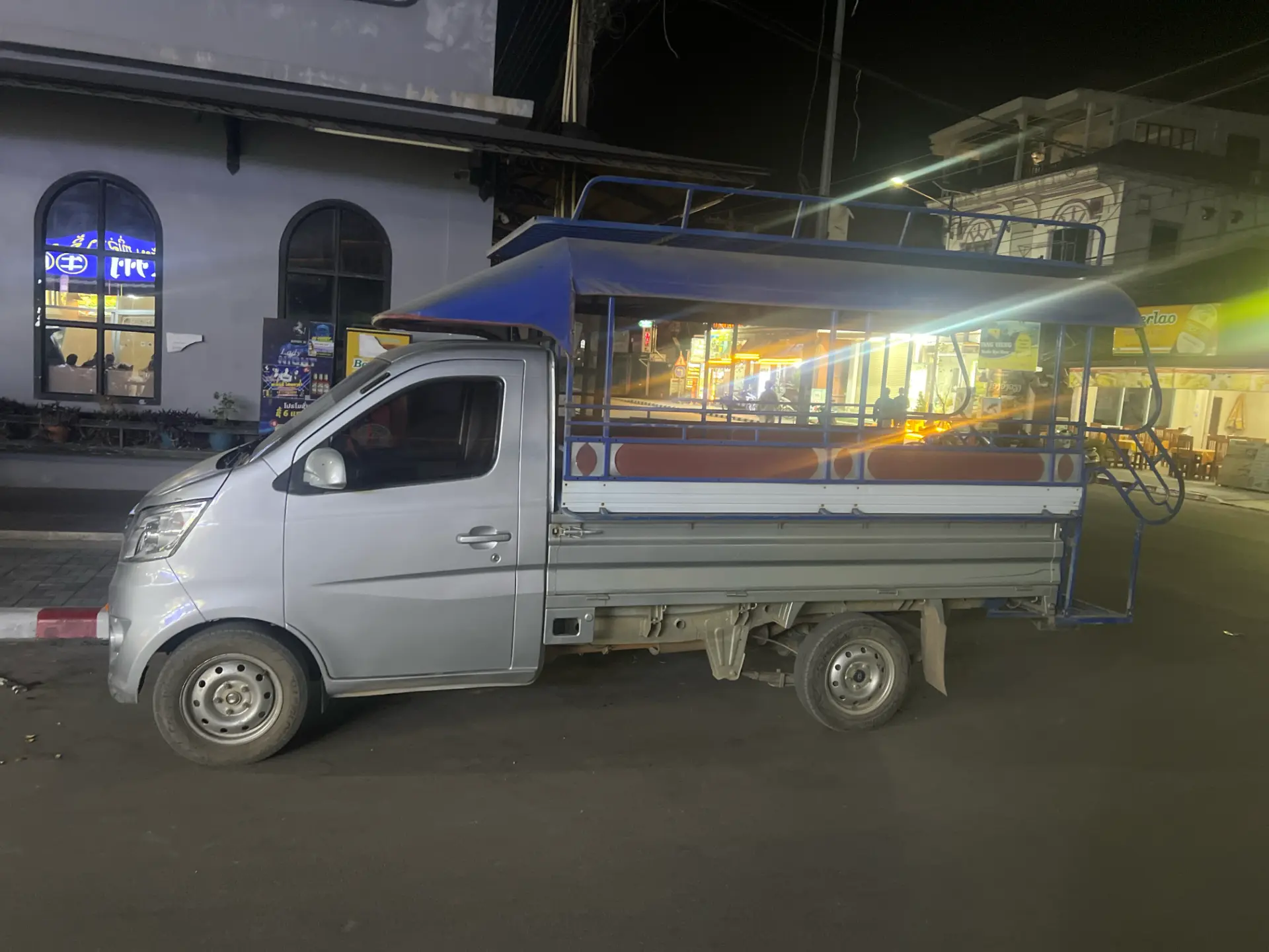 Silver pickup truck with covered blue bench seating used for group transport in Vang Vieng
